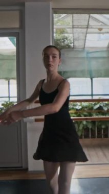 Modern bale stüdyosunda, siyah mayo giymiş, dans teknikleri uygulayan, zarif, genç, beyaz bir balerin resmi.