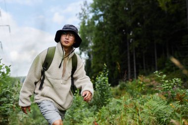 Orta ölçekli, siyah ceketli Asyalı erkek işadamının güneş ışığıyla aydınlanan şehir caddesinde uzaktan çalışırken ince çerçeveli gözlüklerden baktığının fotoğrafı.