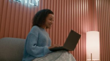 Genç çift ırklı kadın sosyal medya yöneticisinin, marka sosyal ağlarını incelerken dizüstü bilgisayar kullanırken, parlak pembe duvarlı yaratıcı mekanda çalışırken orta boy bir fotoğrafı.