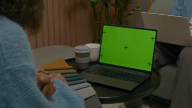 Moda tasarımcılarından oluşan bir ekip, yaratıcı çalışma alanında yeni bir koleksiyon geliştirirken tekstil renk paleti ile etkileşime girerek yeşil ekranlı dizüstü bilgisayarın yanında oturuyor.