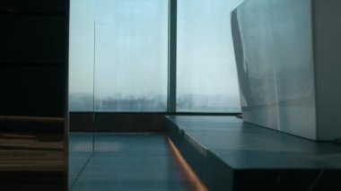 Minimalist, gösterişli bir dairede panoramik pencerelere karşı çıplak ayakla serbest küvete doğru yürüyen ve bornozunu çıkartan, tanınmayacak büyüklükteki bir kadının yan görüntüsü.