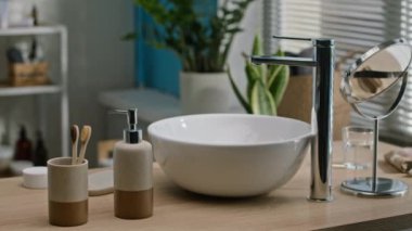 Minimalist banyo tezgahında, parlak seramik leğen, krom musluk, bambu tutacağında çevre dostu diş fırçaları, sabun makinesi, yuvarlak ayna ve arka planda yeşil bitkiler bulunan insanlar yok.