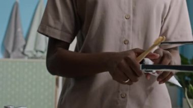 Modern banyoda minimalist tasarım ve doğal ışık tasarımı ile seramik beyaz lavabonun önünde dururken bambu diş fırçasının üzerinde diş macunu sıkan tanınmaz hale gelmiş siyah bir kadın.