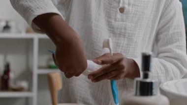 Keten pijama giymiş, dişlerini yoğun bir şekilde fırçalayan parlak banyoda sabah rutinini tek başına yapan neşeli siyahi bir çocuk.