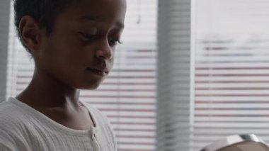 Orta boy siyah çocuğun yuvarlak banyo aynasına bakıp, merakla yansımasını keşfettiği görüntüler.