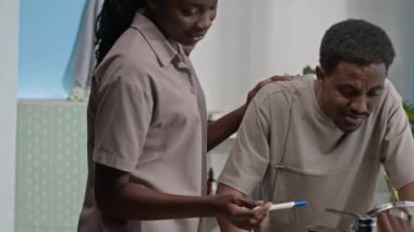 Evli genç siyahi çift, güneşli banyoda lavabonun önünde duruyor. Kadın kocasına hamilelik testi yapıyor.