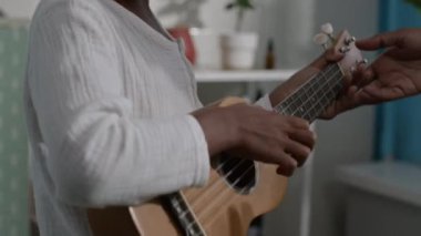 Sabahın erken saatlerinde yumuşak beyaz keten pijamalı, ukulele çalan küçük siyahi çocuğun yakın çekimi.