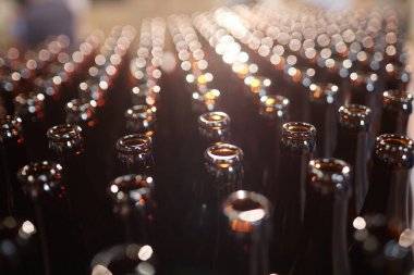 Bira fabrikasındaki üretim hattında parıldayan kahverengi cam şişelerden oluşan düzinelerce şişenin arka plan çekimi.