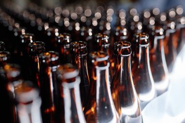 Bira fabrikasındaki üretim hattında ışıkta parlayan düzinelerce açık cam şişenin arka plan çekimi.