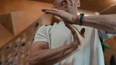 Orta yaşlı, beyaz bir adamın spor giyip, tırmanma merkezinde kapalı alanda antrenman yapmadan önce bileklerini ısıttığı yakın çekim.