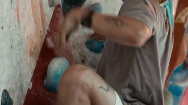 Beyaz tenli genç sporcunun aktif giysi giydiği ve tırmanma ayakkabıları giydiği kayalık spor salonunda kaya tırmanışı yaptığı yakın çekim.