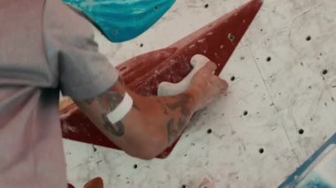 Spor giyimli, spor ayakkabısı giyen ve kaya tırmanışı yapan beyaz tenli genç adamın yakın çekim çekimi.