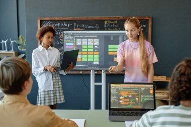 Okul sınıfında bilişim ve programlama üzerine sunum yapan ve dijital ekran kopyalama alanı kullanan iki hevesli genç kızın ön görünüm portresi