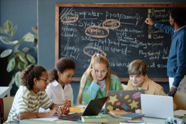 Okul sınıfında birlikte çalışan ve bilgisayar kullanan kafası karışmış bir grup çocuğun cephesi.