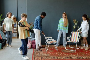 Genç çocukların sahne arkasında podcast ya da video kaydına hazırlanırken öğretmenlerinin yardım ettiği uzun bir çekim.