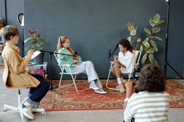 Sahne arkasında podcast yapan veya stüdyoda röportaj yapan ve mikrofonlara konuşan bir grup genç çocuk var.