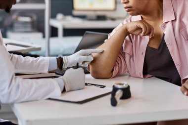 Yandan bakıldığında, eldiven giyen ve cilt döküntüsünü cilt bakımı kliniğinde muayene sırasında hastaların dirseğine işaret eden tanınamayan bir doktor görülüyor.