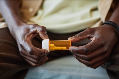 Klinikte yatıp sağlık sorunları ile boğuşurken elinde reçeteli ilaçlarla plastik şişeyle tanınamayan Afro-Amerikan bir adamın yakın çekimi.