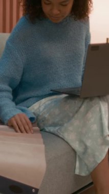 Genç çift ırklı kadın moda analistinin ya da tasarımcının dikey eğimine göre Pastel renk kumaş örneklerini inceleyerek ve dizüstü bilgisayardaki pazarı analiz ederek şık bir çalışma alanında marka yaratmaya çalışırken