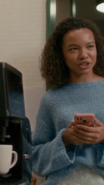 Modern çalışma gününde kahve makinesinin yanında dikey olarak duran iki kadın meslektaşın dostça sohbetlerinin orta boy görüntüsü.