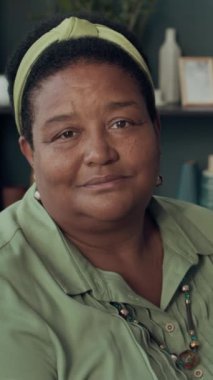 Modern son sınıf Afro-Amerikan kadın portresi şık giyinmiş rahat oturma odasında oturmuş kameraya bakıyor.