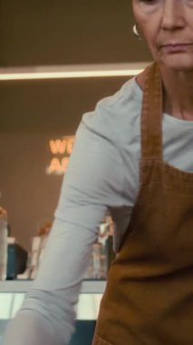 Önlük giyip, deterjan spreyli kafeterya masaları temizleyen Kafkasyalı garson.