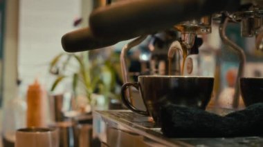 Modern kafedeki kahve makinesinin önünde duran siyah renkli seramik fincana yakın çekim, espresso ile dolduruluyor.