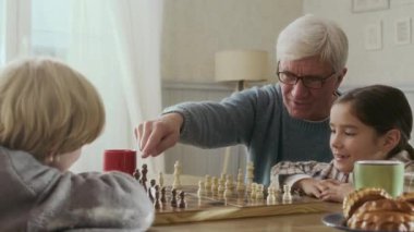 Gri saçlı, gözlüklü yaşlı bir adamın göğsü. İki akıllı torunu ile satranç oynuyor. Gündüz vakti rahat bir ev ortamında, ahşap masada.