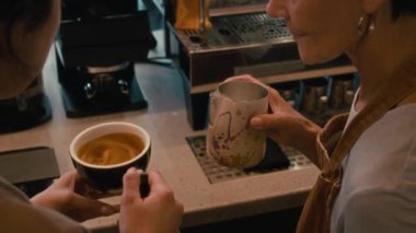 Yeni çalışana cappuccino yapmayı öğreten tanınmayacak kadar deneyimli bir baristanın yüksek açılı görüntüsü.