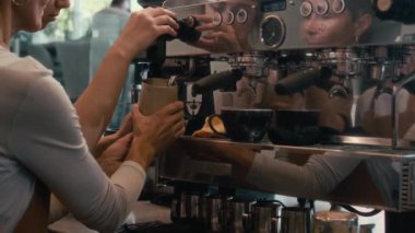 Genç deneyimli barista, kahve makinesini kullanarak yeni çalışana sütünü nasıl hazırlayacağını öğretiyor.