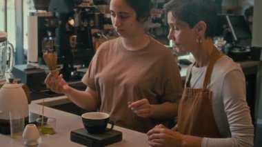 Genç bayan barista kıdemli kafe işçisine matcha çayı yapmak için chasen aletini nasıl kullanacağını öğretiyor.