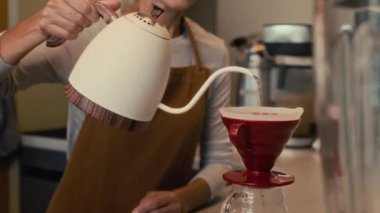 Kafkasyalı kıdemli barista modern kafede damlatan kahve yapıyor, kaynamış suyu kabın içine döküyor.