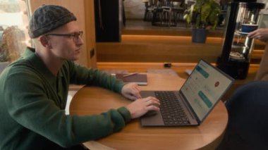 Tanımlanamayan garson laptoplu beyaz bir erkeğe bir fincan cappuccino getiriyor.