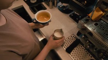 Kafede bir fincan kapuçino yapan tanınmayan genç bayan baristanın yüksek açılı görüntüsü.