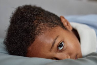 Küçük siyahi çocuğun evde yatakta yatarken yüzünde merak ifadesiyle kameraya bakıp uzayı kopyaladığı yakın plan.