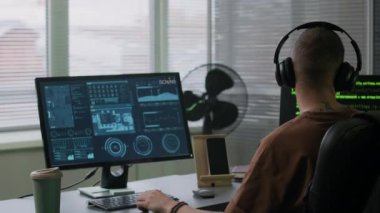 Akşamları modern ofisteki bilgisayar ekranında kompleks veriler üzerinde çalışırken kulaklıkla müzik dinleyen Kafkas bilişim uzmanı