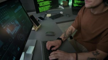 Kolları dövmeli, rahat genç beyaz erkek programcı. Kulaklıkla müzik dinlemenin keyfini çıkarırken aynı zamanda arka planda dizüstü bilgisayarında program kodları çalıştırıyor.