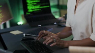 Ağır çekimde, gece modern programcılar ofisinde bilgisayar masasında oturan, gözlük takan, günlük giysi programlama kodu takan, ciddi, çift ırklı, genç bir bilişim uzmanı görülüyor.