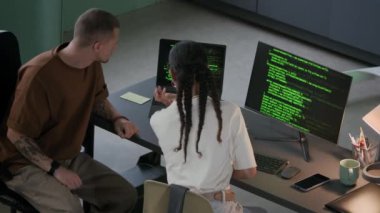 Bilgisayarın ve bilgisayarın önünde oturmuş, modern ofiste program kodlamasını tartışan ve onunla çalışan genç programcıların yüksek açılı arka plan görüntüsü.