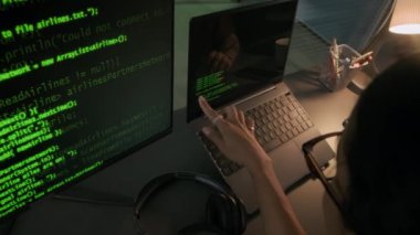 Gözlüklü genç bir kadın programcının dizüstü bilgisayarın ve bilgisayarın önünde oturmuş ve gece kollarında dövme olan erkek arkadaşıyla program kodlarını tartışırken yüksek açılı görüntüsü.