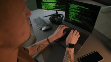 Bilgisayarında dövmeli kolları olan beyaz erkek programcının masa lambasını ekranda çalışan program koduyla kapatarak mesaisini gece ofisinde bitirdiği yakın plan görüntüsü.