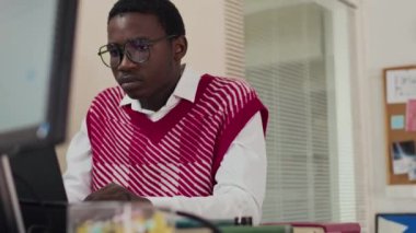 Modern ofis ortamında, modern ofis ortamında, kitaplar ve dijital aletlerle çevrili, şık kırmızı ve beyaz süveter ve gözlük giymiş genç bir adamın beli.