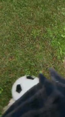 Yeşil çimenlikte futbol topunu tekmeleyen, çimenlerde futbol antrenmanı yapan, sıradan giyinmiş, tanınmayan genç oyuncunun dikey görüntüsü.