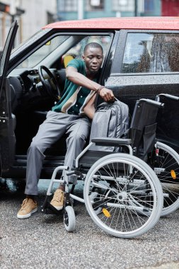 Engelli genç Afrikalı Amerikalı adamın dikey portresi direksiyona geçiyor ve katlanabilir tekerlekli sandalye kullanıyor.