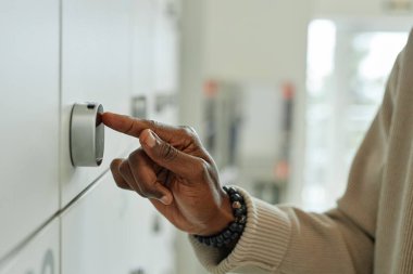Afro-Amerikalı erkek ofis çalışanının kişisel eşyalarını çağdaş çalışma alanına depolayan akıllı dolapların dijital tuş takımına girerken yan görünümü