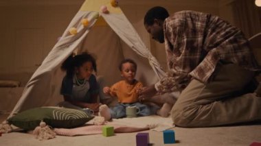Afrika kökenli genç bir Amerikalı baba bebeğiyle ilgilenirken marşmelovlu kakaodan parmaklarını yalarken akşam vakti küçük kız kardeşiyle güzel bir odada, rahat bir ışıkla çadırda otururken.