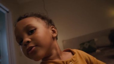 Küçük Afro-Amerikan bir çocuğun kendini videoya kaydettiği görüntüler. Yatak odasının penceresinin önünde duruyor. Küçük kız kardeşi de bulanık arka planda.