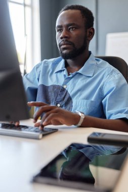 Kentte tekerlekli sandalye kullanan Afro-Amerikalı bir adamın dikey yan görüntüsü ve beyaz duvar fotokopi alanına karşı rampada ilerleyişi.