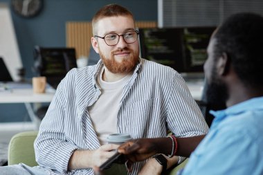 Modern ofiste sohbet eden iki meslektaş. Bir adam kahve fincanı tutarken diğeri tartışırken