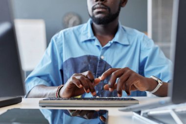 Modern ofis ortamında bilgisayarda çalışırken klavyede yazan Afrikalı Amerikalı bir adam çalışma alanı yüzeyinde yansıyan ışığı görebilir